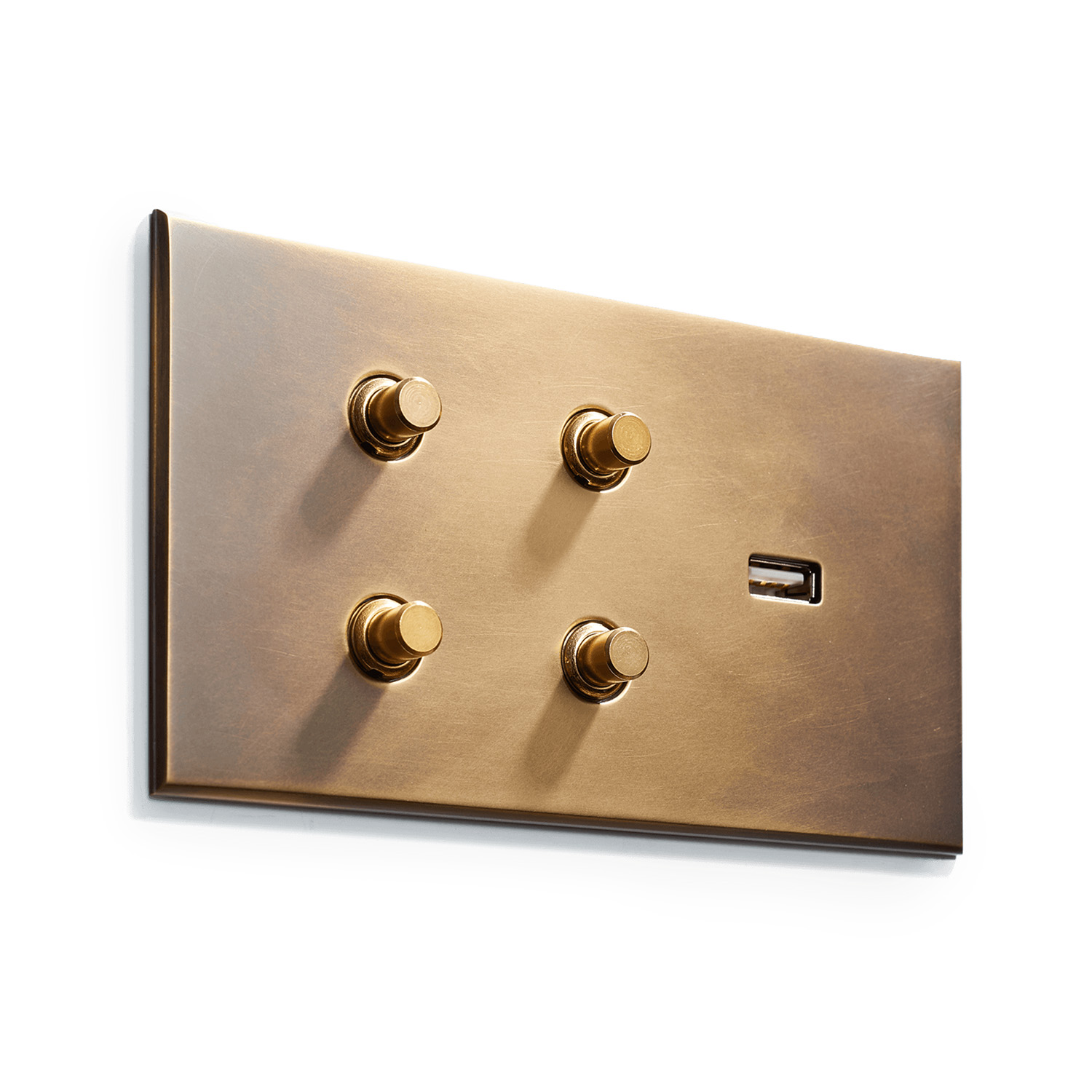 A polished brass electrical switch panel with four round knobs and a toggle switch, mounted on a white wall. the finish is smooth and reflective, giving a luxurious appearance.