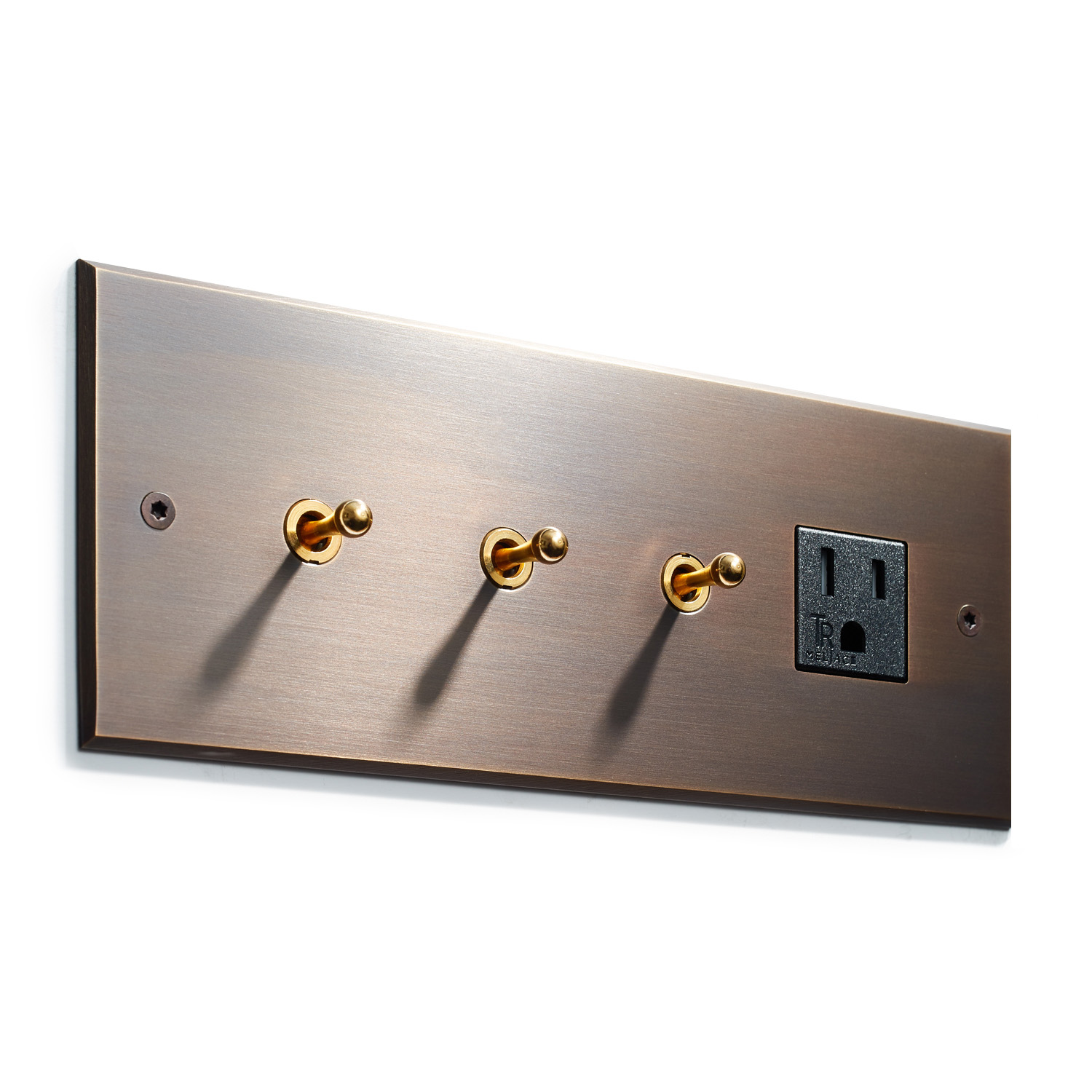 Brushed metal wall plate with three toggle light switches and one electrical outlet, casting soft shadows on a light-colored wall.
