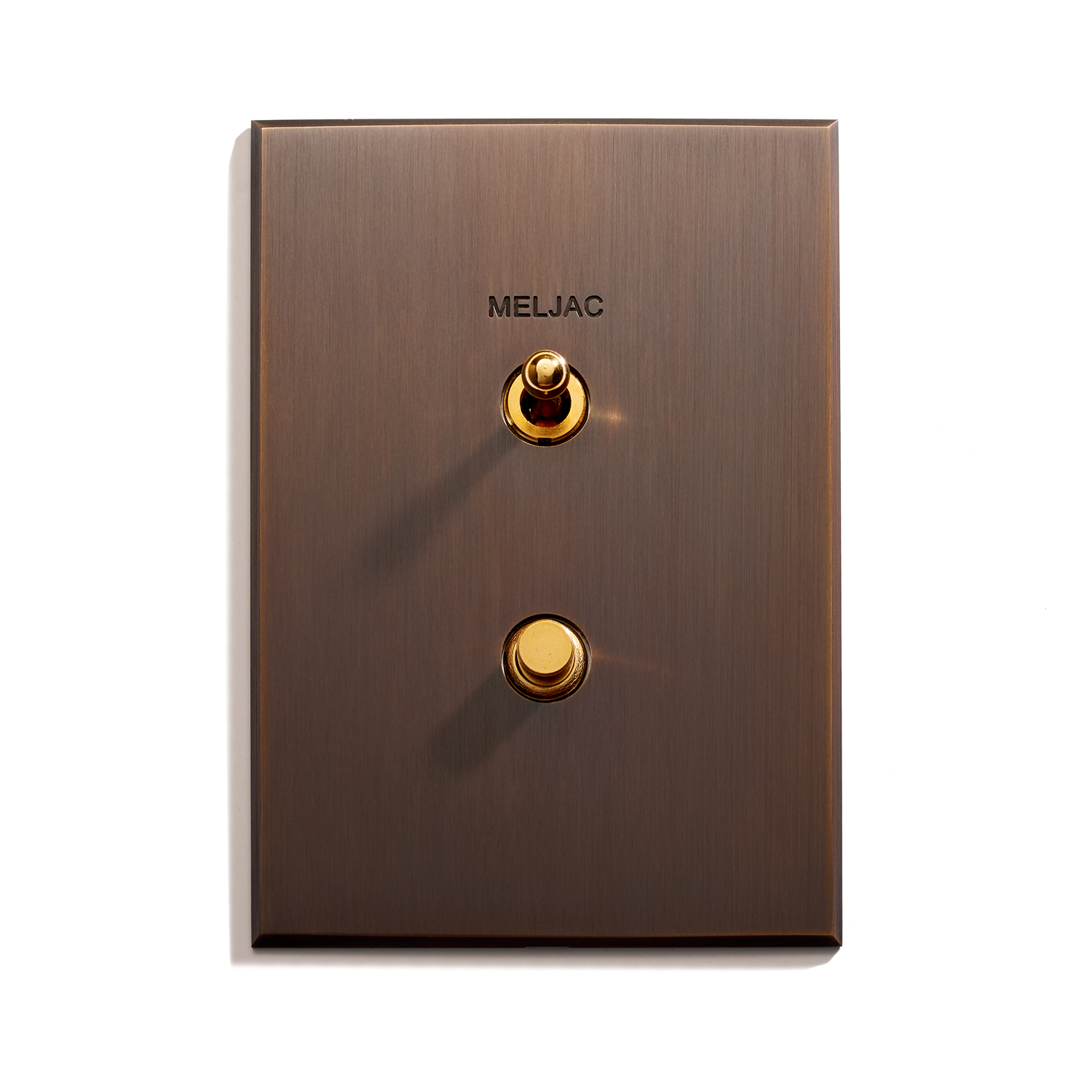 A rectangular, bronze-colored metallic light switch panel features two toggle switches. The top smaller toggle switch and the larger bottom toggle switch are both gold. The panel has rounded corners and the word "MELJAC" is engraved near the top switch.