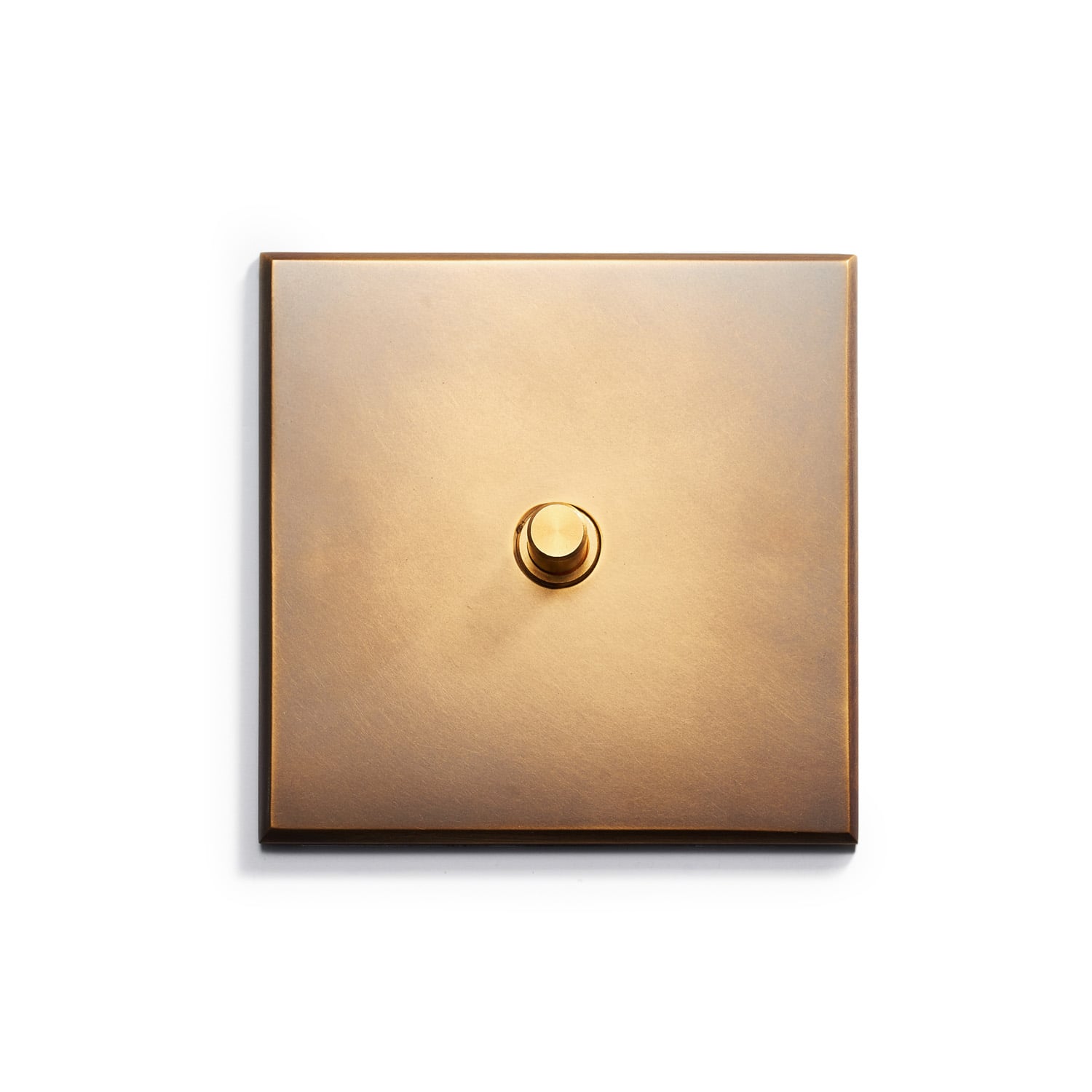 A square brass light switch on a white surface.