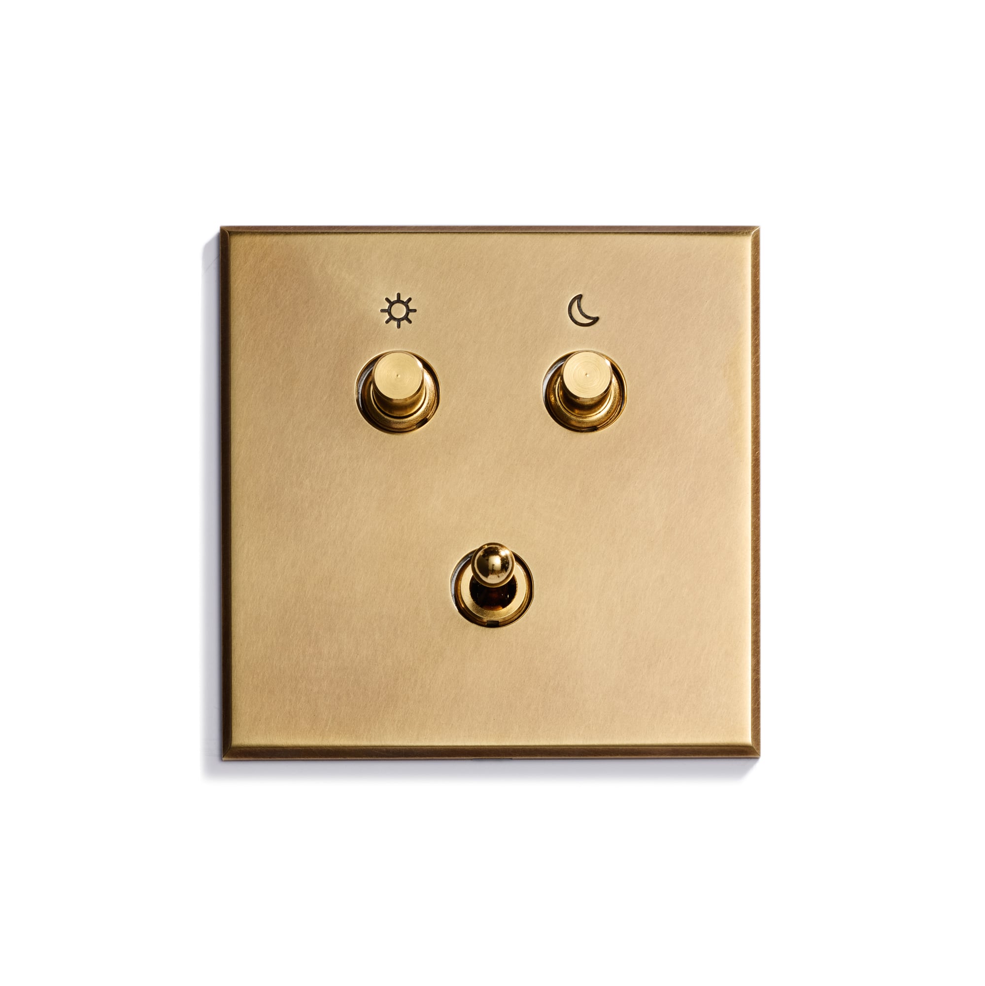 A brass light switch panel with three toggle switches; the top left switch is marked with a sun icon, the top right with a moon icon, and the bottom switch has no icon.