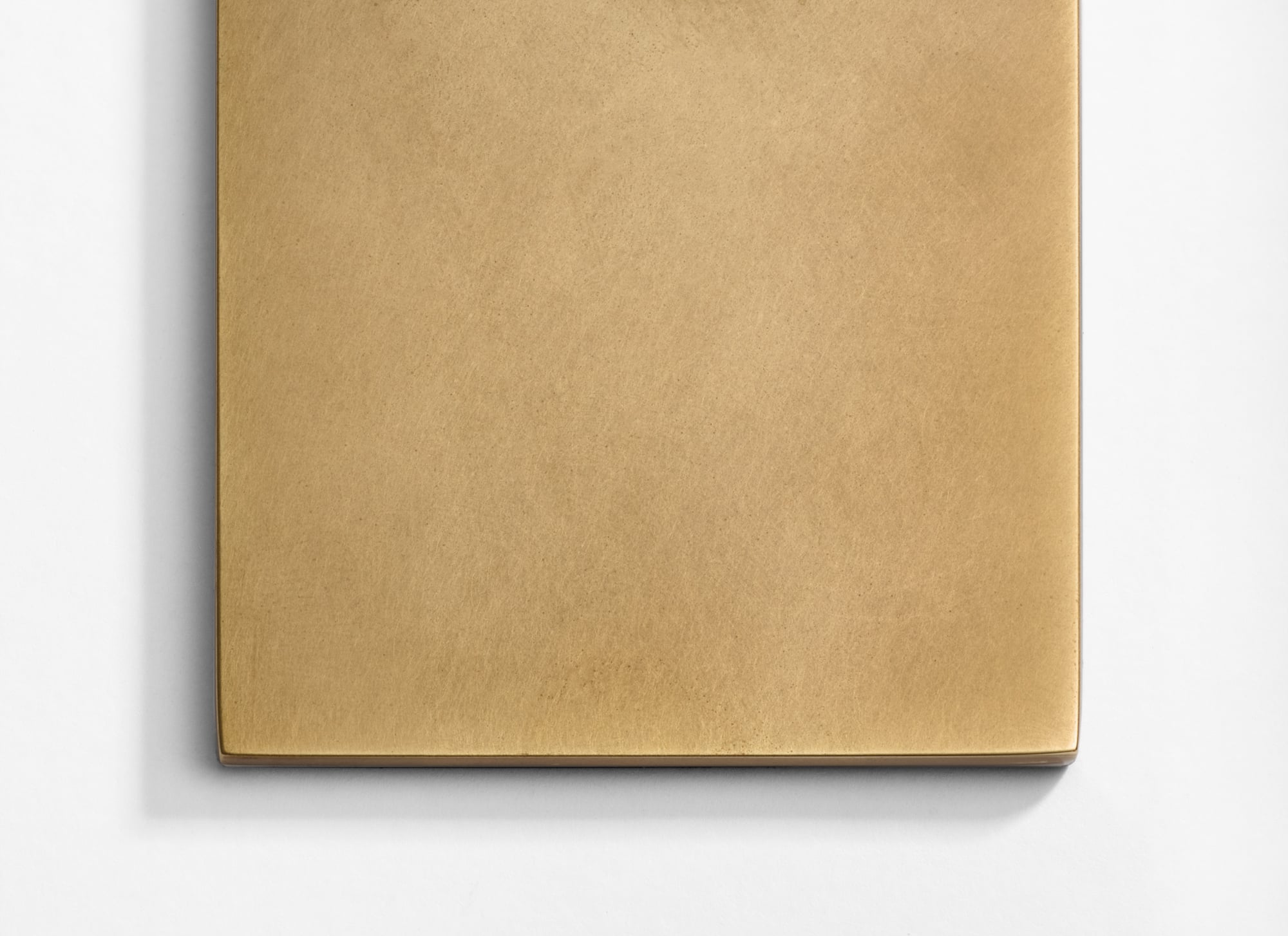 A close-up photo of a rectangular, flat, brass-colored metal plate with a smooth, matte surface and slightly rounded edges, placed on a white background.