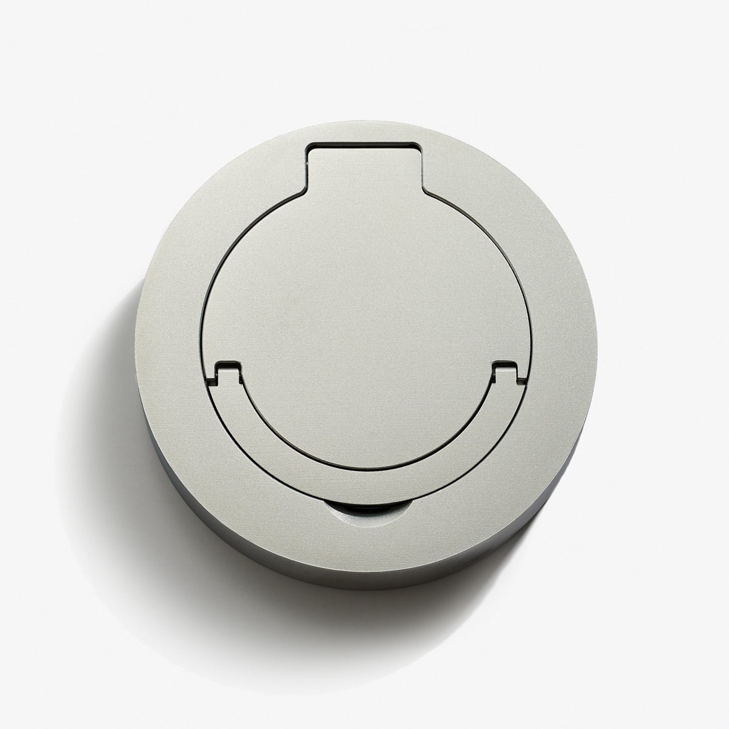 A grey, round object resembling a compact and minimalist device cover or lid, featuring a cylindrical shape with a simple, sleek design. The smooth surface includes a cut-out pattern extending partially from the edge to the center. The object is placed on a white background.