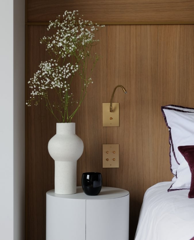 A white bed with a vase of flowers next to it.