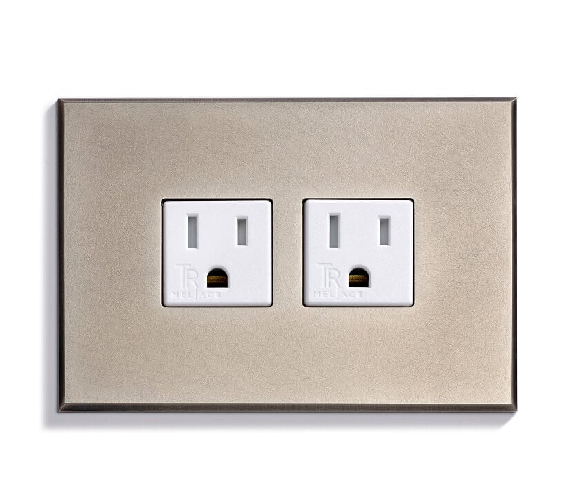 A close-up view of a wall plate with two white electrical outlets set in a brushed metal frame against a white background.