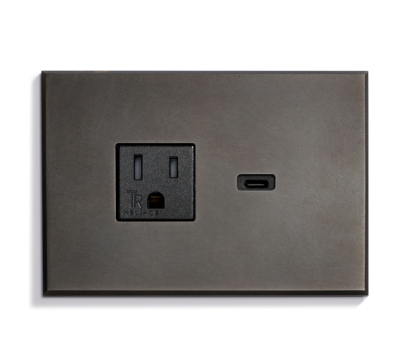 A dark metallic wall plate features one standard three-prong electrical outlet on the left and one USB-C port on the right, both set on a smooth, minimalist surface.