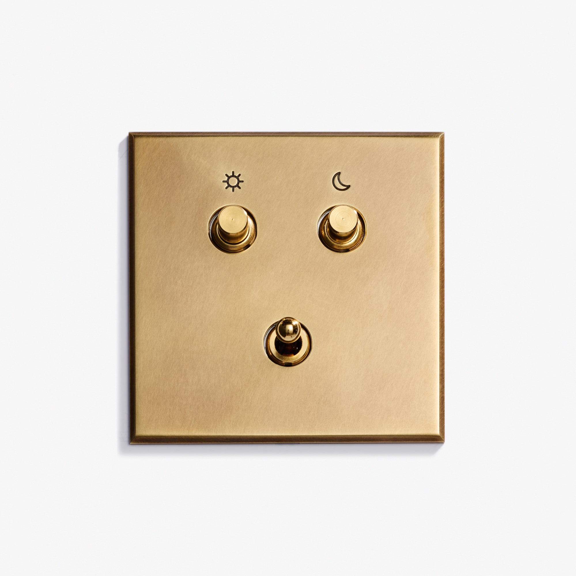 A gold-colored Classique Keypad 82 x 82 light switch panel with three toggle switches: the top left marked with a sun symbol, the top right with a moon, and one unmarked switch centered below them.