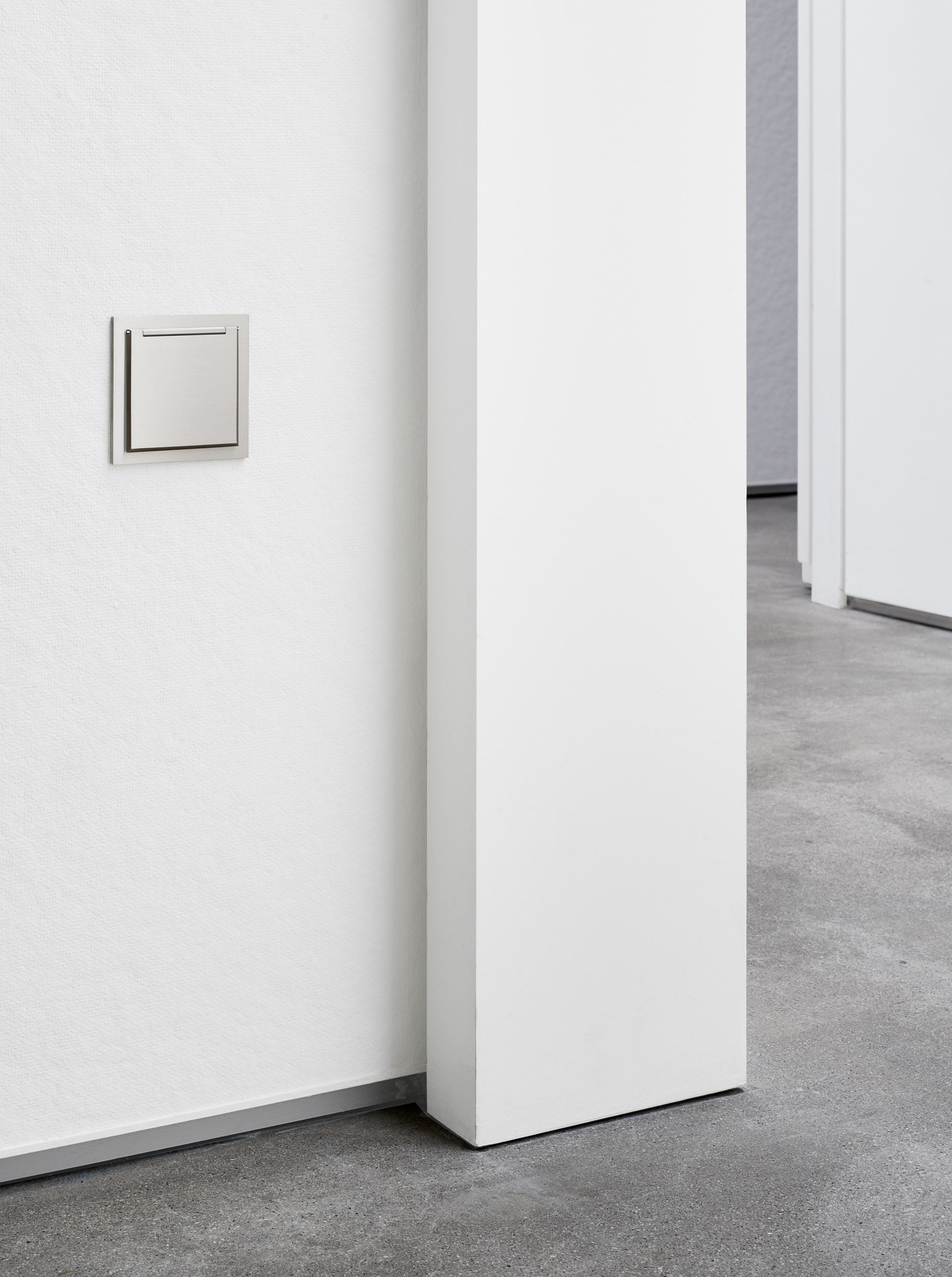 A white wall in an empty room with a light switch.