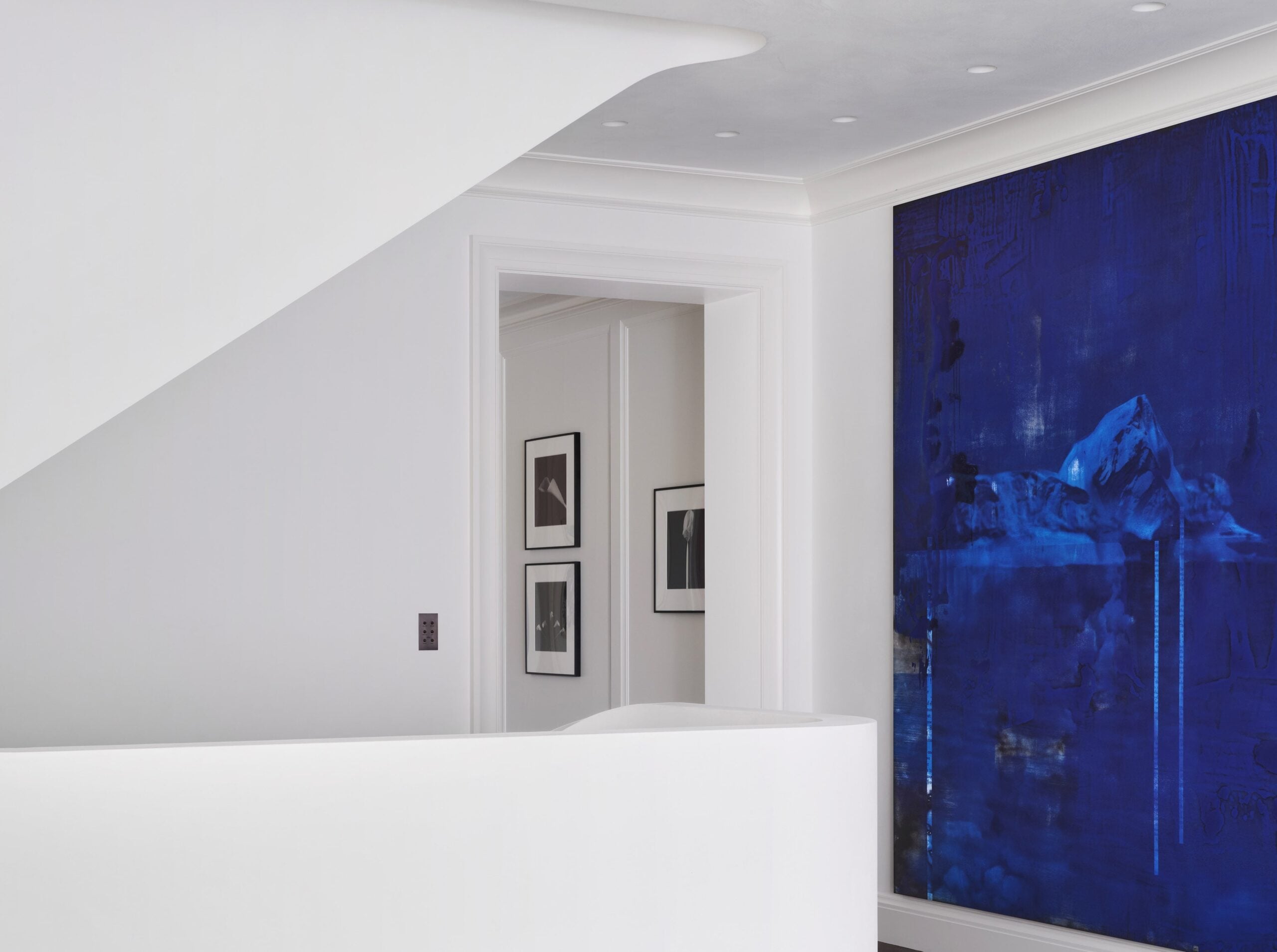 A blue painting hangs on a wall in a white home.