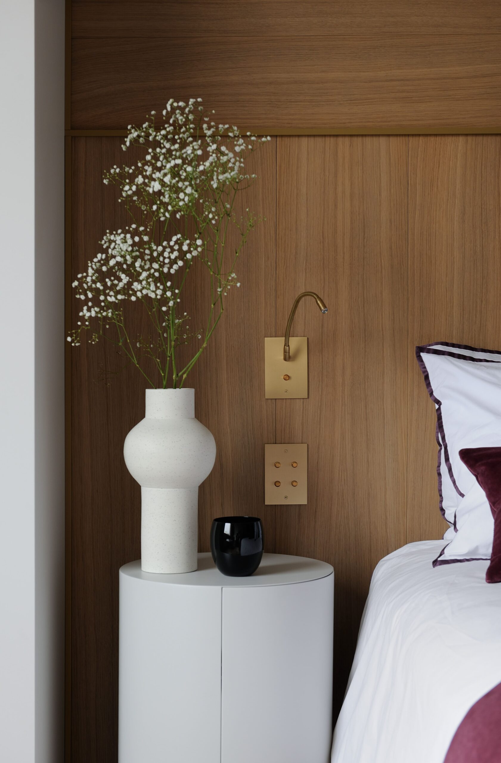 A white bed with a vase of flowers next to it.