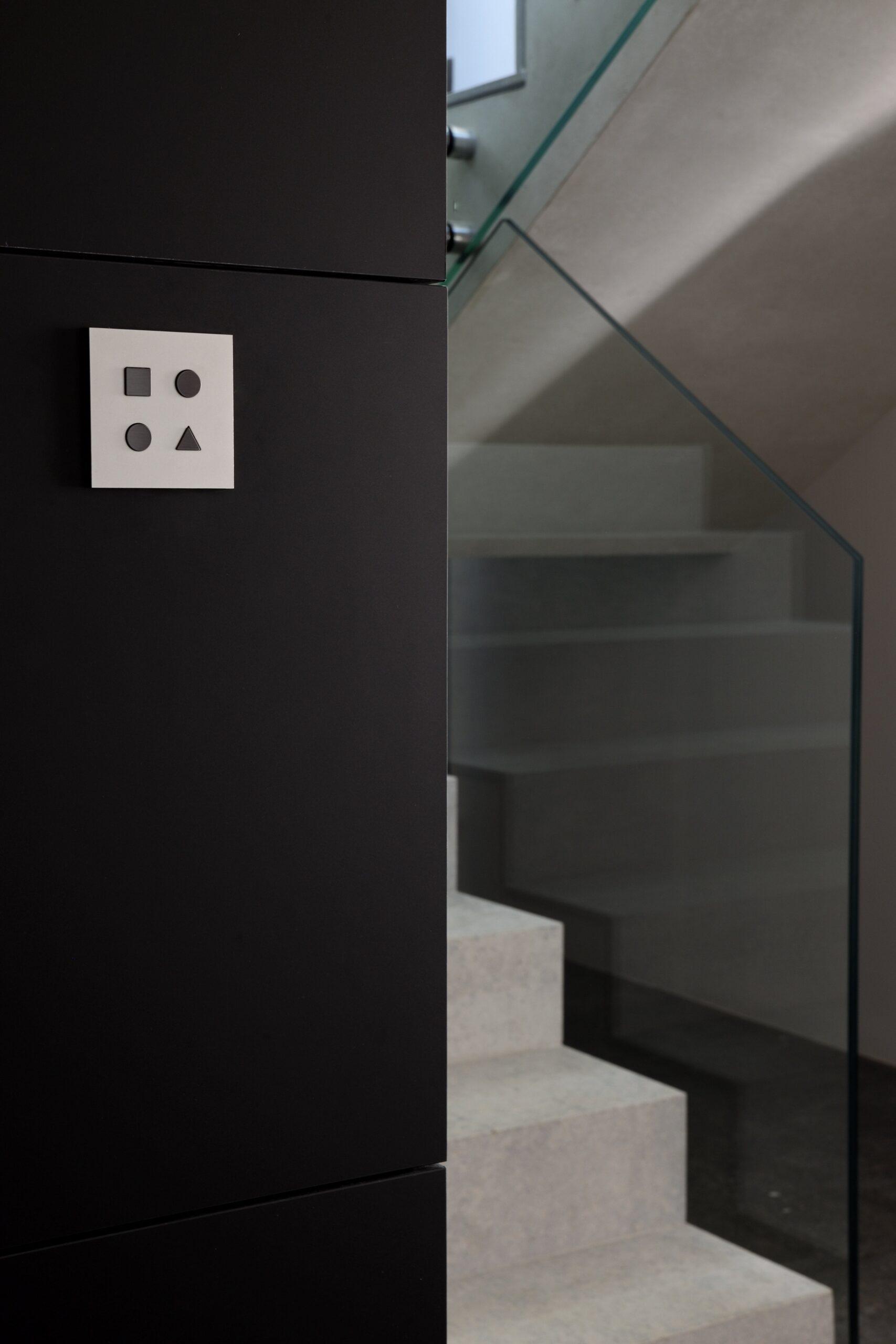 A black wall mounted light switch with a stairway in the background.