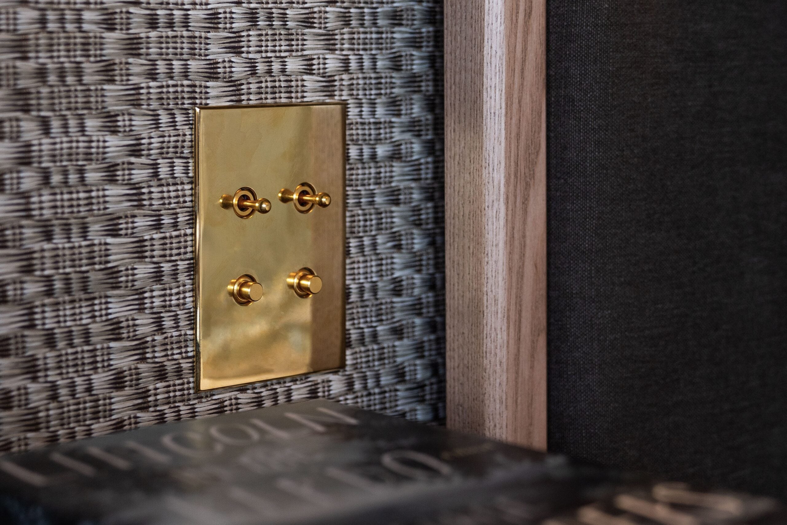 A brass light switch on a wall next to a book.
