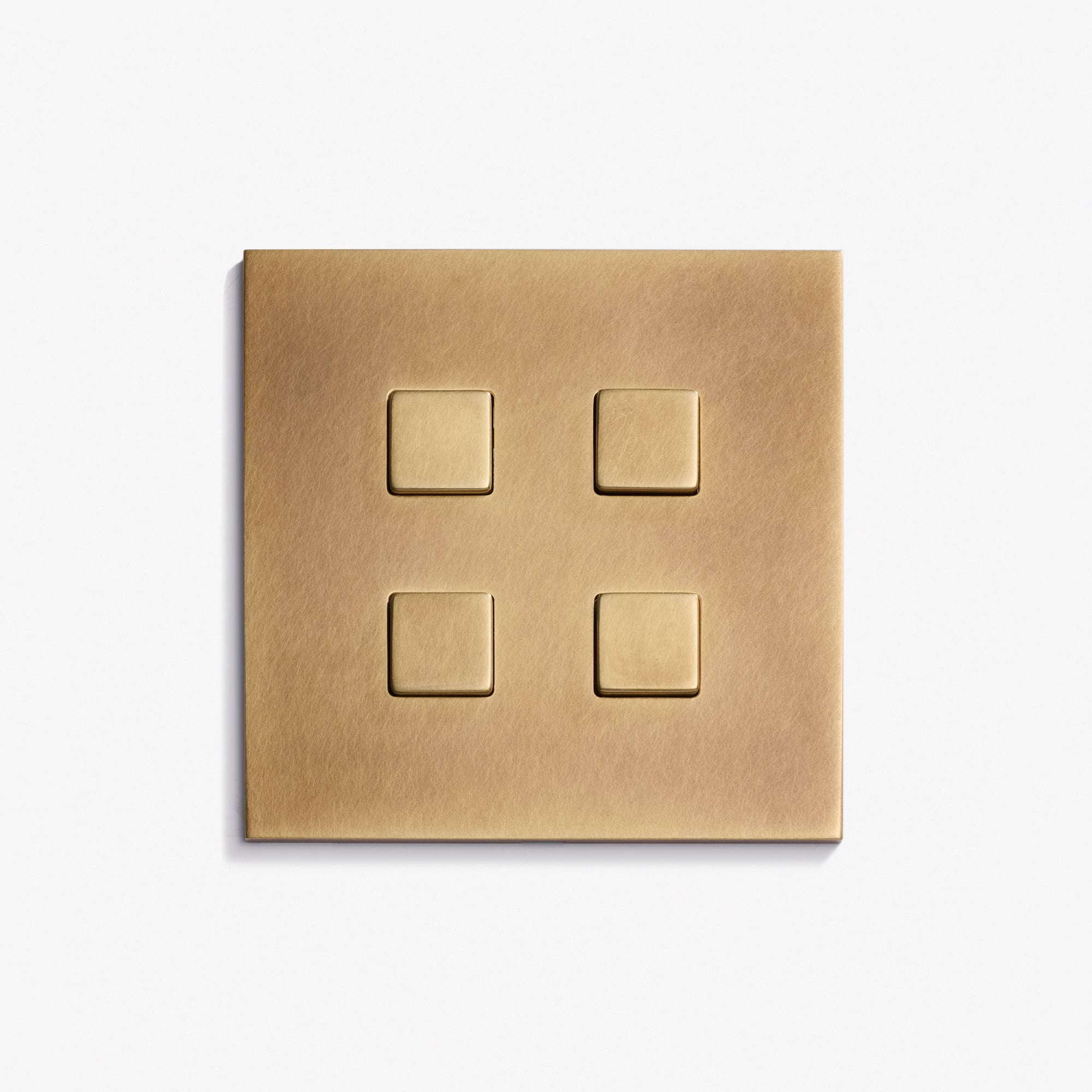 A Damier Keypad 82 x 82 brass light switch plate features four evenly spaced square buttons, mounted on a plain white wall.