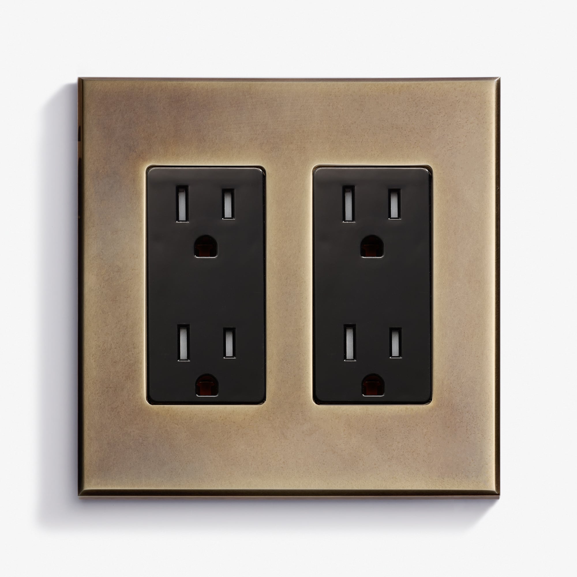 A brass wall plate with two black electrical outlets, each with two sockets, mounted on a white background.
