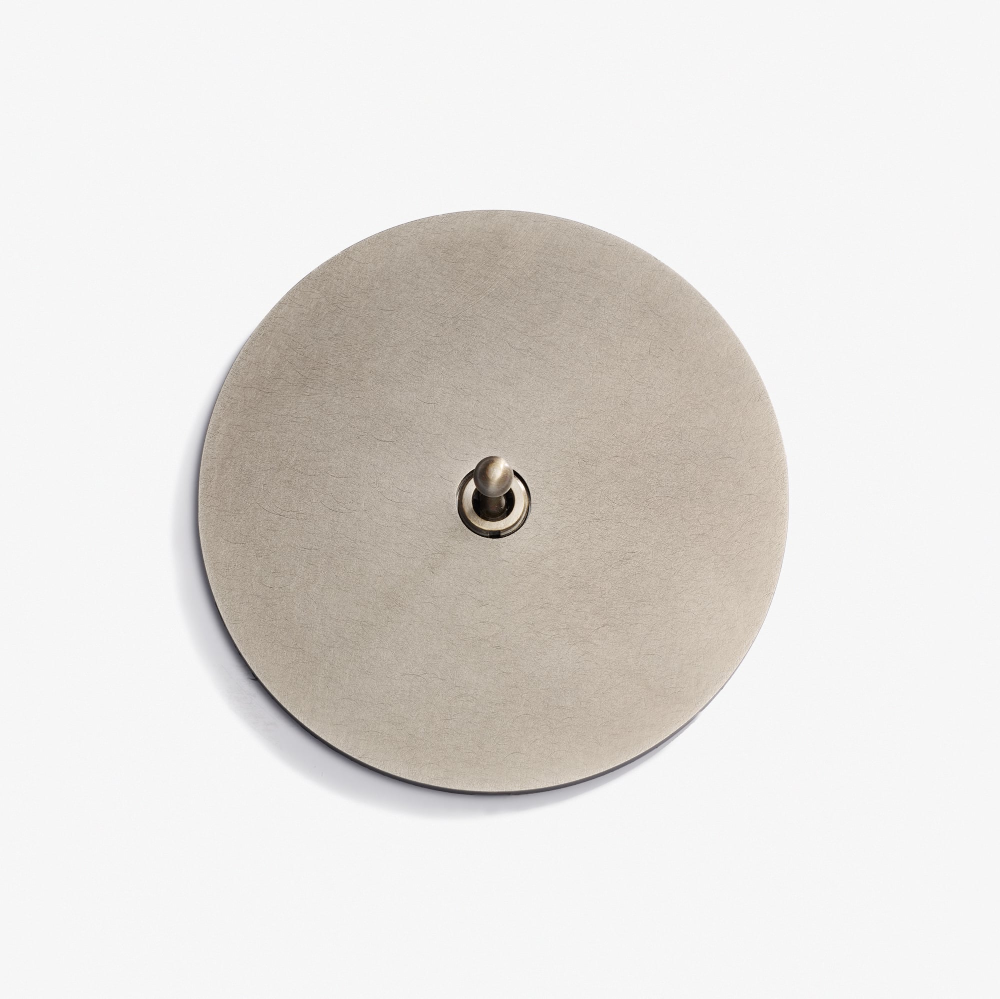 A round, flat, brushed metal plate with a small toggle switch in the center, reminiscent of the refined design found in the Classique Keypad 98D, set against a plain white background.