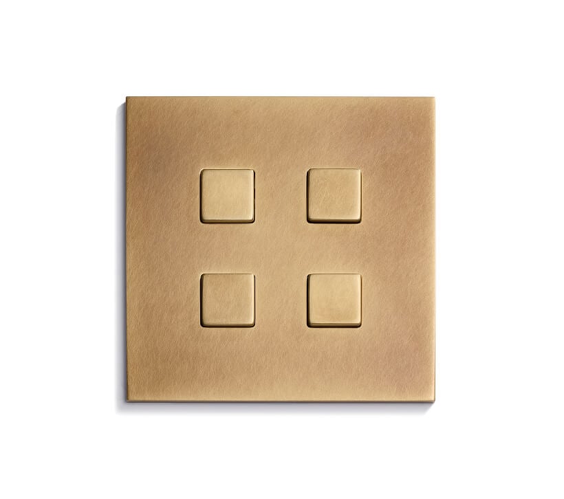 A square, brushed brass light switch plate with four square buttons arranged in a 2x2 grid, mounted on a white background.