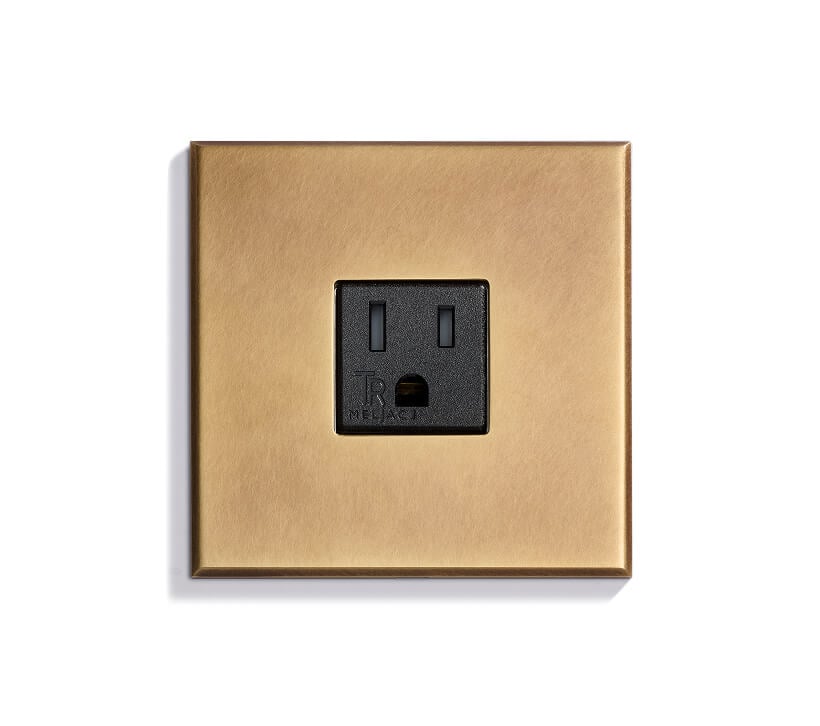A single black electrical outlet set in a square, brushed gold wall plate against a white background.