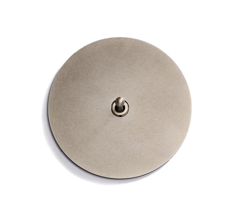 A round, flat, metallic object with a small, raised cylindrical knob at its center, photographed against a white background.